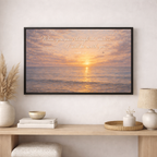 Framed artwork with sunset over water and text on a wall above a wooden console table.