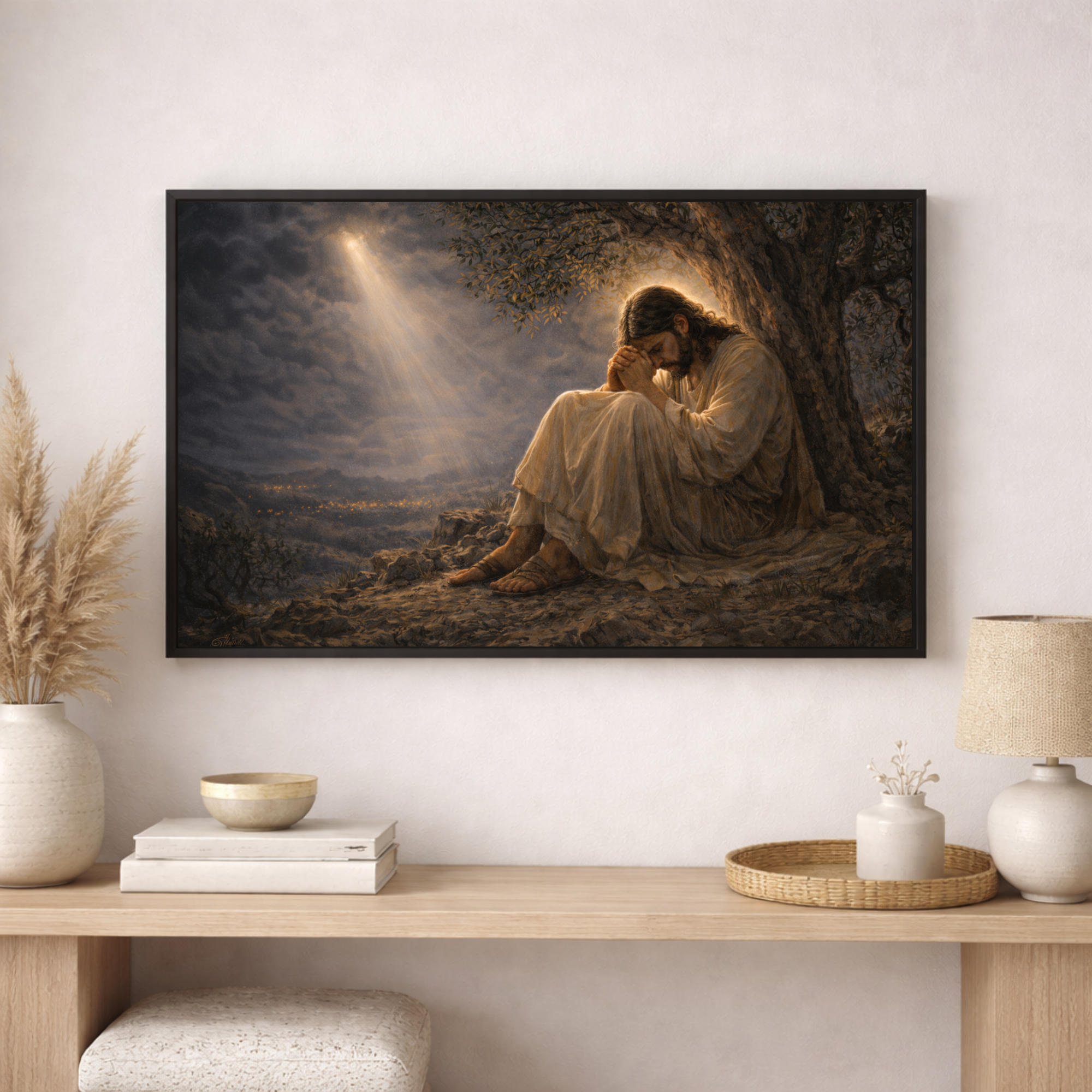 Framed artwork of a religious figure sitting under a tree with a light shining on it, displayed in a room with decor elements.